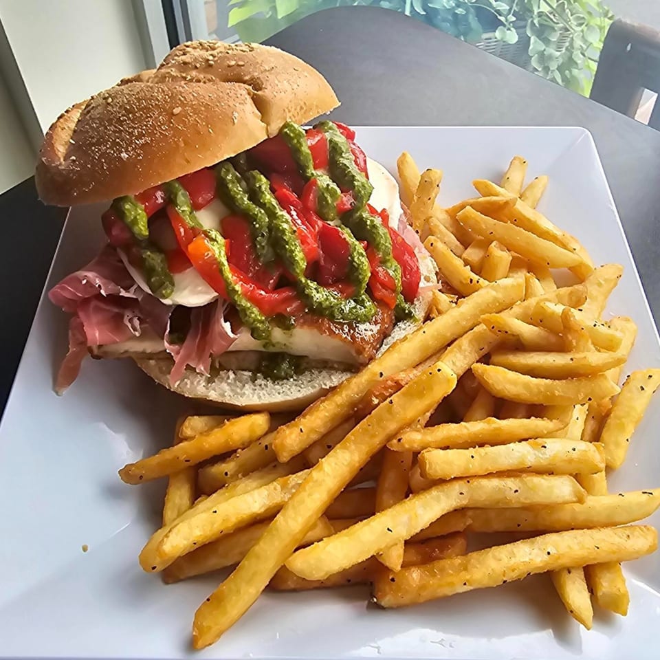 A chicken sandwich with prosciutto, mozzarella, roasted red peppers, and pesto, served with fries.