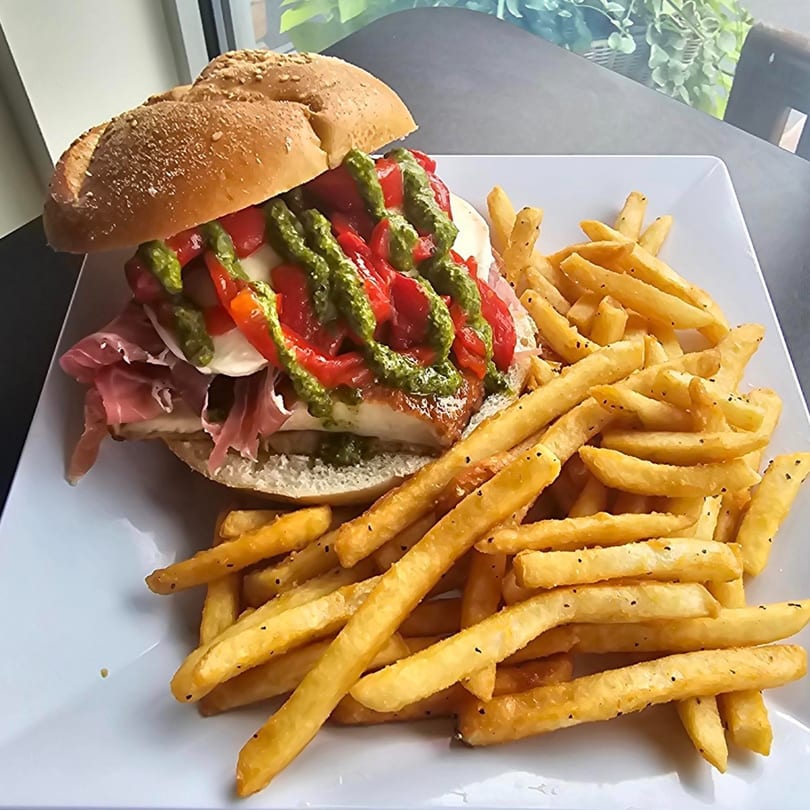 A chicken sandwich with prosciutto, mozzarella, roasted red peppers, and pesto, served with fries.