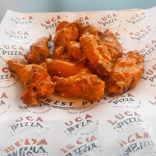 Luca Pizza's buffalo wings, coated in a vibrant orange sauce, served on branded paper.