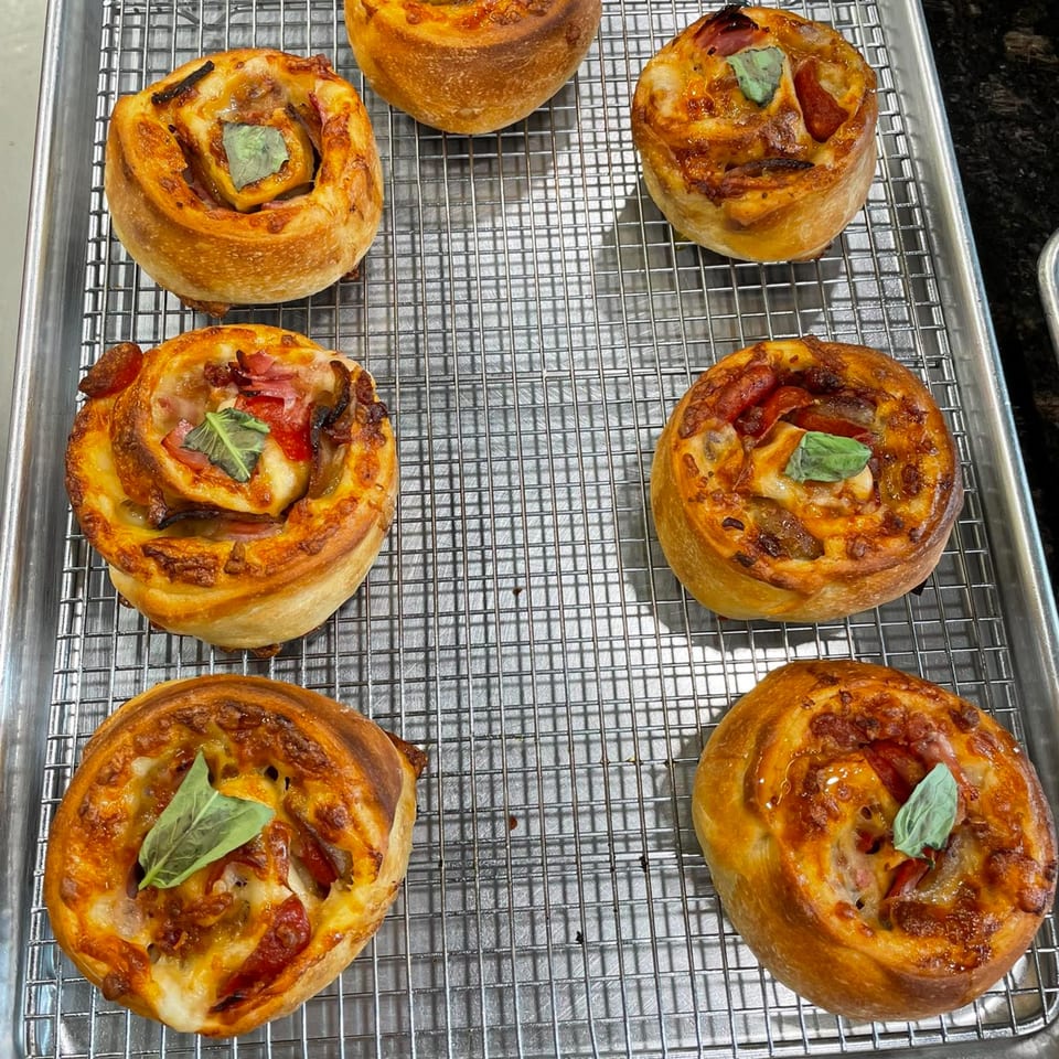 Seven golden-brown pizza rolls with melted cheese, pepperoni, and basil leaves on a cooling rack.
