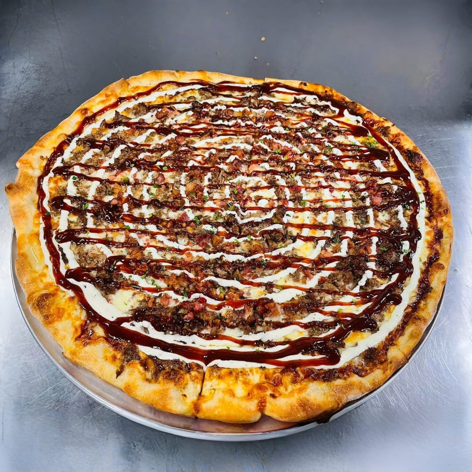 Large pizza with a thick crust, topped with meat, white sauce, and BBQ sauce drizzle.