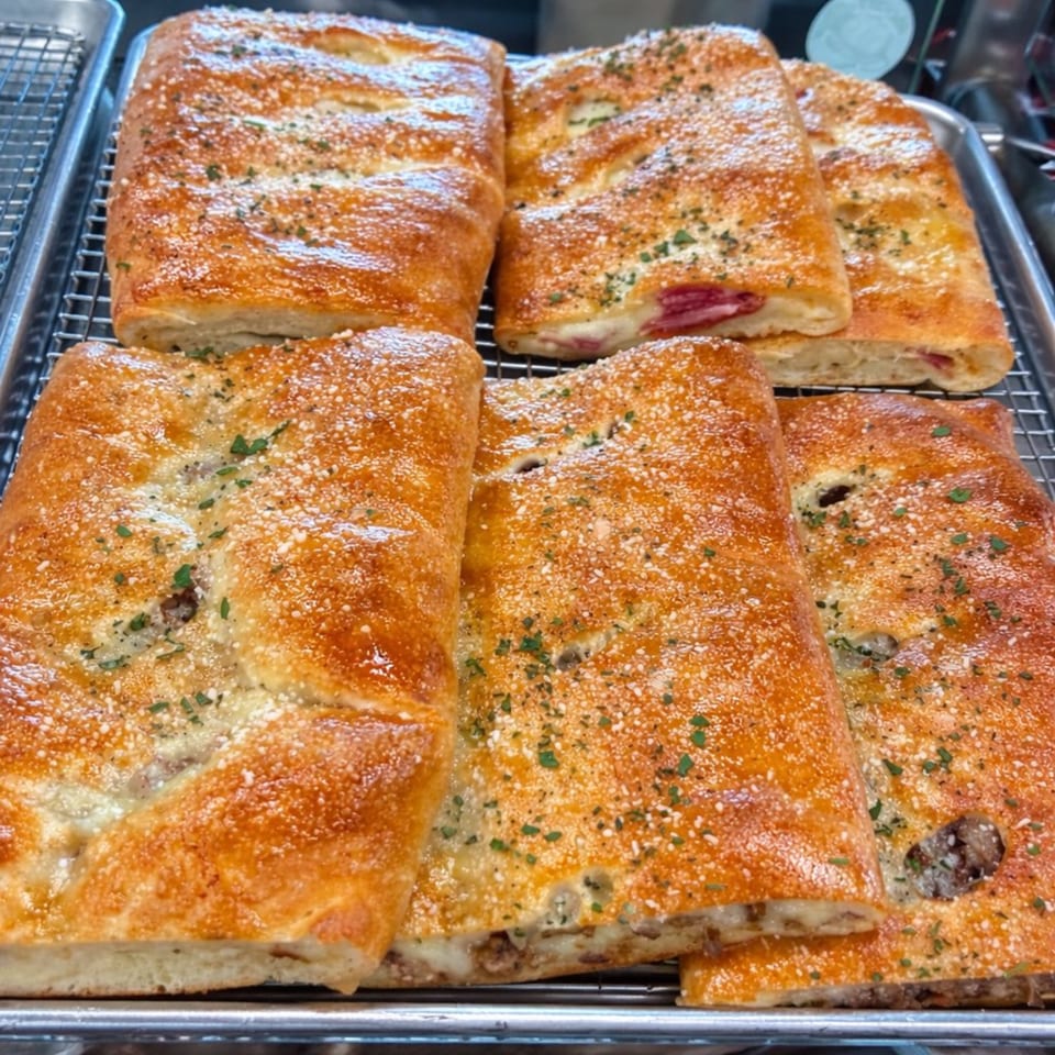 Golden-brown calzones, some with visible meat and cheese fillings, on a metal cooling rack.